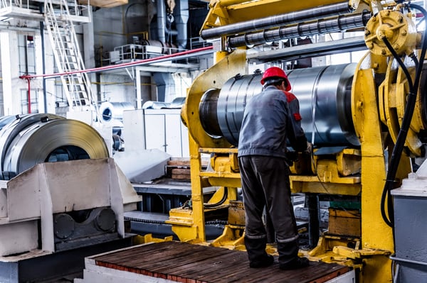 Worker and stock with rolls of sheet steel in industrial plant